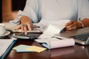 Alt: Persona trabajando con calculadora, laptop y documentos en un ambiente de oficina, enfocada en gestión administrativa y servicios de instalaciones industriales.