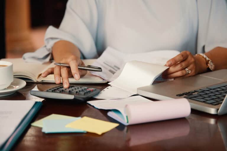 Alt: Persona trabajando con calculadora, laptop y documentos en un ambiente de oficina, enfocada en gestión administrativa y servicios de instalaciones industriales.