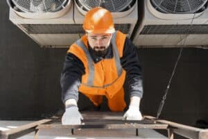 Alto trabajo en instalación y mantenimiento de sistemas HVAC, con técnico usando equipo de protección personal en una escalera en un espacio industrial.