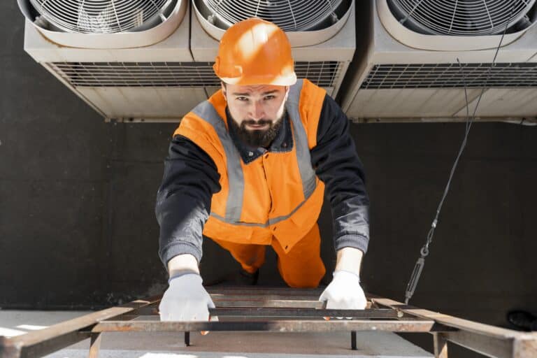 Alto trabajo en instalación y mantenimiento de sistemas HVAC, con técnico usando equipo de protección personal en una escalera en un espacio industrial.