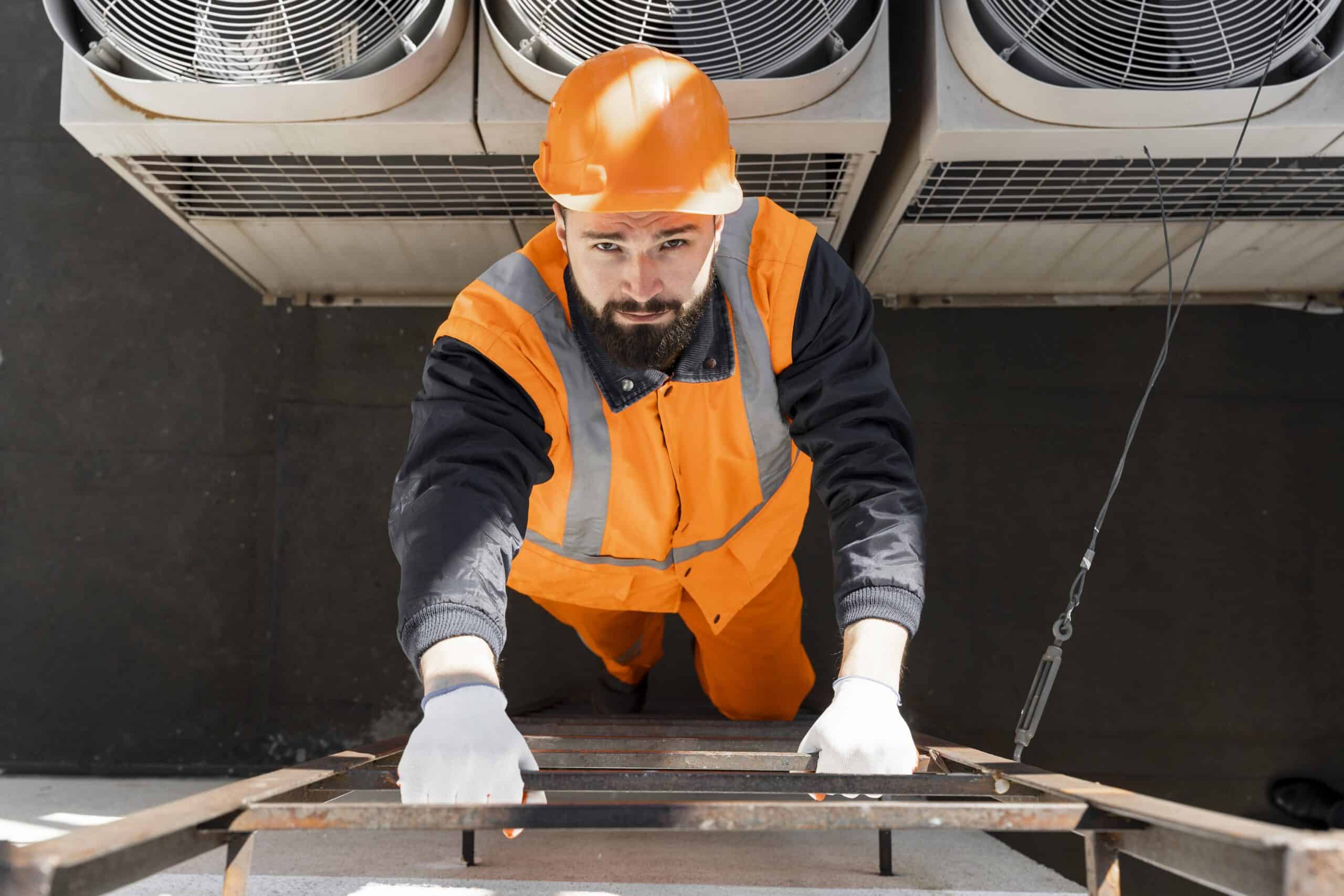 Alto trabajo en instalación y mantenimiento de sistemas HVAC, con técnico usando equipo de protección personal en una escalera en un espacio industrial.