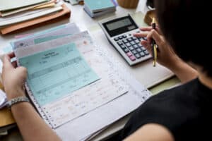 Contador revisando facturas y documentos financieros en oficina, utilizando calculadora y bolígrafo para gestionar pagos y trabajos administrativos, en un entorno de trabajo eficiente.