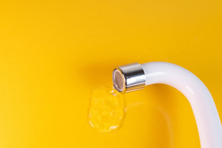 Boca de fregadero con agua cayendo sobre fondo amarillo.